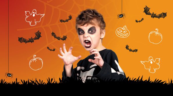 Child dressed up for Halloween with white face and black etes and lips surrounded by graphics of bats, ghosts and pumpkins on a orange background with black grass at the bottom