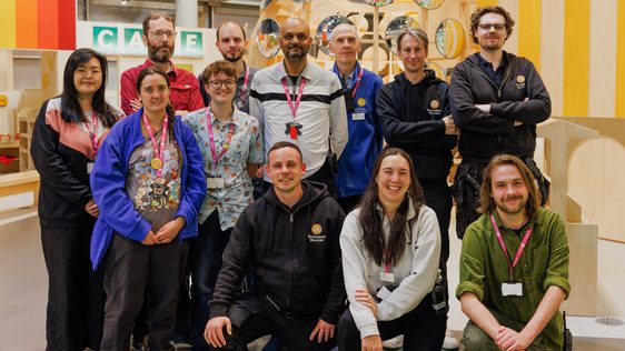 A group of staff standing and kneeling, they all wear pink landyards and are smiling.