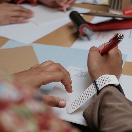 A persons hands drawing on a piece of paper at a table.