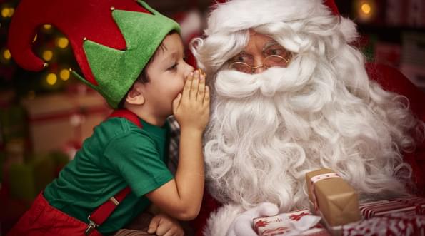 A child dressed as an elf whispering into Santa's ear.