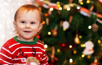 Young boy wearing Christmas jumper in front of Christmas tree