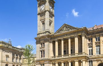 Photo ofshowing the front of Birmingham Museum and Art Gallery. The tall clock tower of the building is surrounded by blue sky.