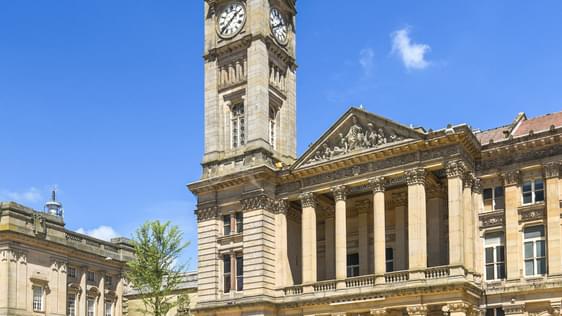 Photo ofshowing the front of Birmingham Museum and Art Gallery. The tall clock tower of the building is surrounded by blue sky.