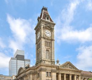 A view of the clocktower that is part of the Birmingham Museum and Art Gallery building. It is seen against a backdrop of blue sky with clouds.