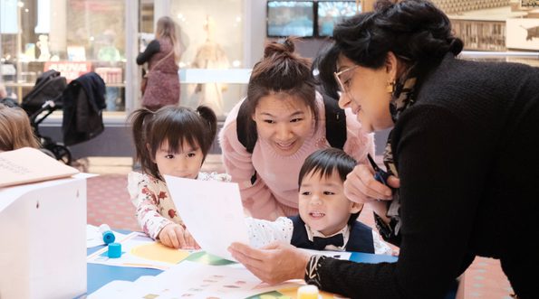 Adults and children looking at paper resource while doing a craft activity.