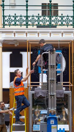 Staff members installing an object on display using a lift and ladders.