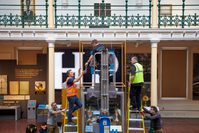 Staff members installing an object for display using a small crane and ladders.
