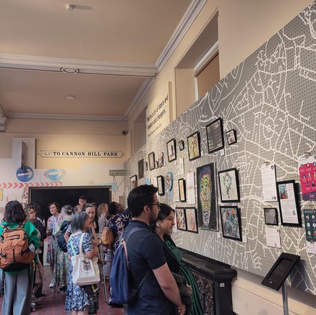 Image shows a group of visitors viewing the Carers Voice display which includes poetry, artwork and self-portraits.