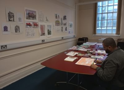 An artist is sitting at a table with a folder of William Blake artworks in front of him.