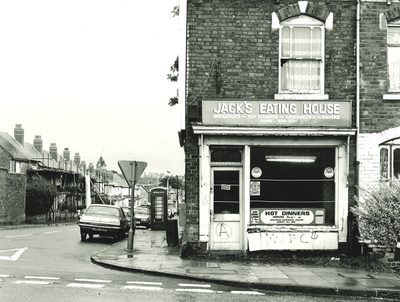 Black and white photo of the exterior of a cafe on a street corner.