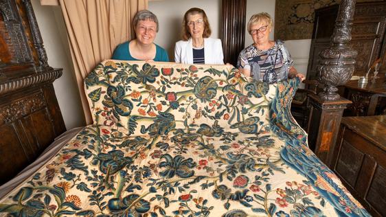 Three ladies holding a17th century restored embroidered bed hanging
