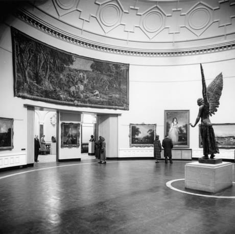 Old black and white photography showing the Round Room gallery. The bronze statue of Lucifer can be seen standing on a white plinth. Lucifer is facing the entrance to the gallery.
