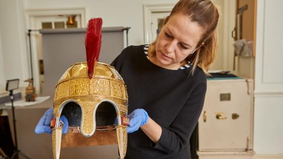A lady wearing blue conservation gloves holding a gold replica Anglo Saxon helmet