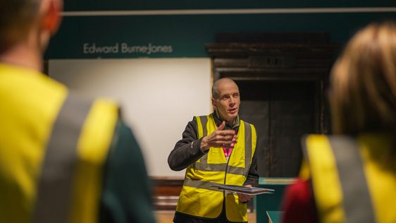 A person wearing a high visibility jacket talking to two people with their backs to the camera.