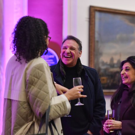 Three people in a gallery smiling and talking in an art gallery.
