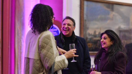 Three people in a gallery smiling and talking in an art gallery.