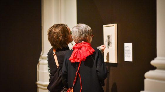 Two people looking at an artwork on the wall through a small magnifying glass.