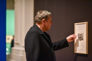 A person looking at an artwork on display using a magnifying glass.