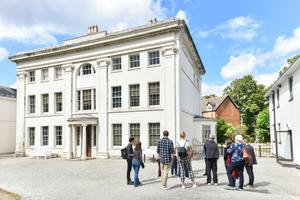 The white Georgian building Soho House is shown with a group of visitors standing in front of ot. The house is three stories high with many windows.