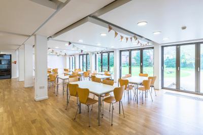 Tables and chairs set up in a room. The wall is made up of glass doors annd you can see the grass outside through them.