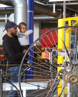 A man holding a small child while looking at historic bicycles on display.