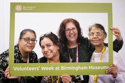 Four smiling women pose together holding a frame that reads "Volunteers' Week at Birmingham Museums".