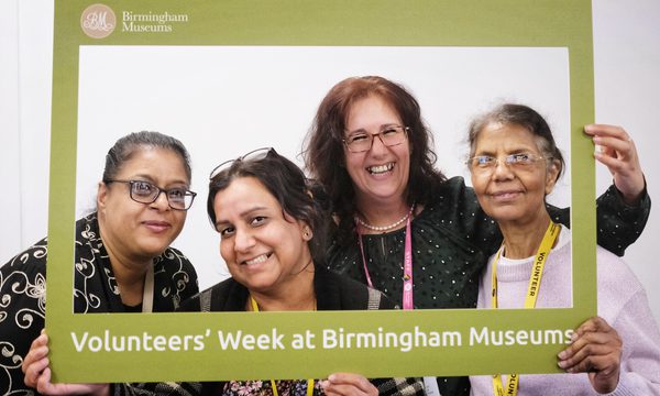 Four smiling women pose together holding a frame that reads "Volunteers' Week at Birmingham Museums".