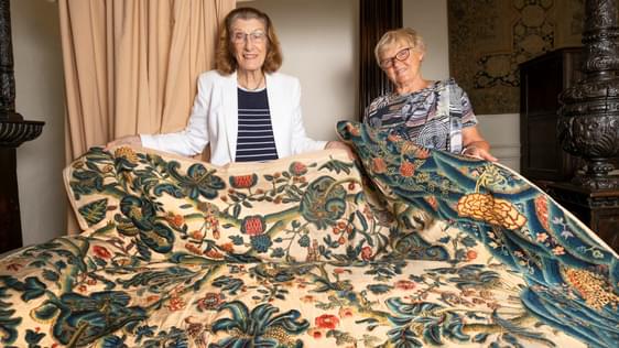 Two ladies holding a restored 17th century embroidered bed hanging