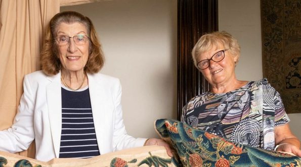 Two ladies holding a embroidered bedspread.