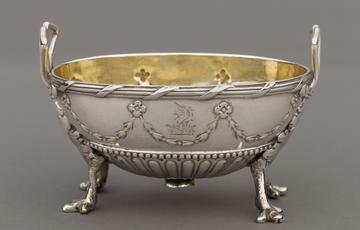 Silver container shaped like half an egg, ornately decorated with four claw feet and two handles