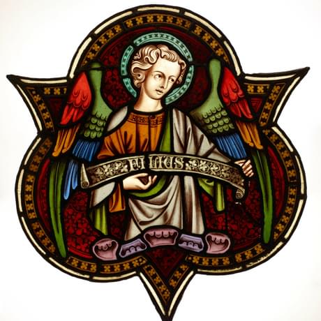 Stained glass window trefoil of an angel with multicoloured wings holding a scroll with the Latin word 'Filus'