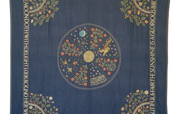 Square embroidered bed cover, with a poetic quote around the edges, a rainbow at each corner, a circle pattern in the middle with a sun at its centre, divided into 8 panels with animals of the day and night and flower and plant motifs