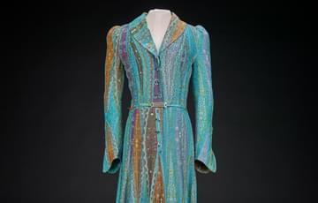 Long dress in blue patterned fabric, with long sleeves and a shawl collar, button fastenings at the front