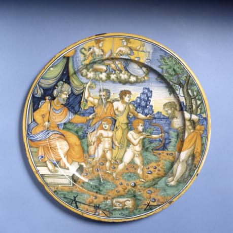 Round, ceramic plate painted with a scene depicting a fabled scene of two boys with bows and arrows, one is shooting at the body of his dead father while a judge  watches