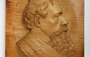 Wooden plaque with carved, profile portrait of author Charles Dickens