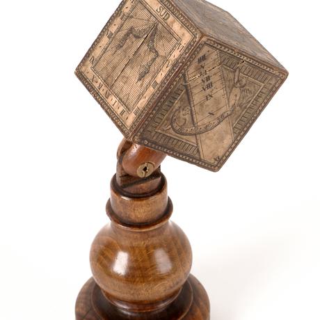 Turned stand with a cube covered in printed paper numerals mounted on the top