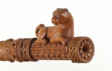 Ornately carved stick with a figure of a pug-like dog on the top