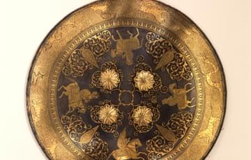 Round steel shield overlaid with gold patterns of animals and four mounted figures