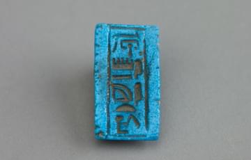 Small, blue pottery plaque with ancient hieroglyphic writing down the middle