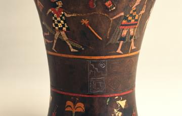 Wooden drinking cup, without handles, the top is wider than the base. It is painted with an abstract pattern around the middle, human figures and birds above, flowers below
