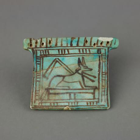 Small glazed rectangular piece of pottery with outline image of a jackal-headed deity in front of a pyramid