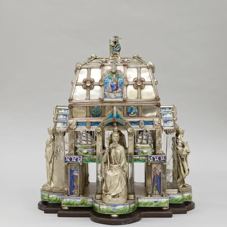 Very ornate silver box sitting on a plinth featuring four silver figures, glass columns and enamelled pictures of various scenes
