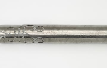 Piece of metal, pointed at one end, shaped to resemble a giant pen nib