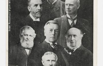Black and white postcard with a photo montage image of portraits of seven men in suits