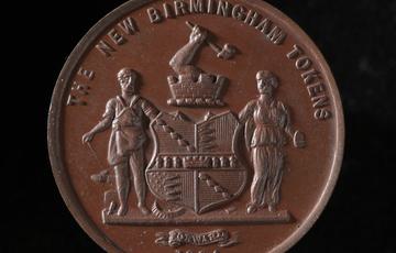 Brown coin with a coat of arms, two figures standing either side and an arm holding a hammer emerging from a turret above