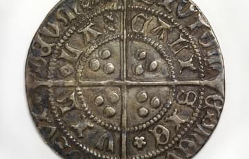 Dark coin with  cross pattern dividing it into quarters there are letters and symbols arranged in a concentric pattern