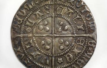 Dark coin with cross pattern dividing it into quarters there are letters and symbols arranged in a concentric pattern
