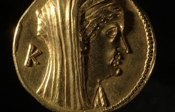 Gold coloured coin with the bust of a robed figure looking to the right, their eyes are closed