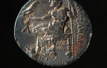 Misshapen dark coin featuring a man sitting down and a bird perched on his arm