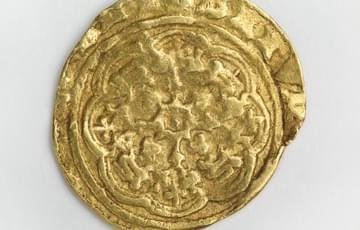 Misshapen gold coloured coin with a flower inscribed